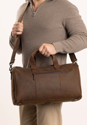 Rudos odinės kelioninės kuprinės su dviem rankenomis ir nuimama petneša. Priekyje yra užtrauktuku užsegama kišenė ir kniedėmis sustiprinti dugno akcentai.