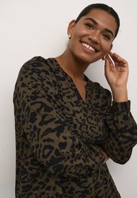 Bluse mit Leopardenmuster in Braun und Schwarz, mit V-Ausschnitt, langen Ärmeln und gerippter Textur. Das Design umfasst einen dezenten Glanz und eine lockere Passform.