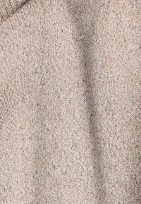 Lichtbeige gebreide stof met een zachte textuur, gekenmerkt door een mix van tan en crèmekleurige vezels met een subtiel gespoten patroon.