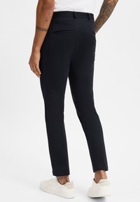 Marineblaue Hose mit schmaler Passform, ausgestattet mit Gesäßtaschen und subtiler Textur, kombiniert mit weißen Sneakers.