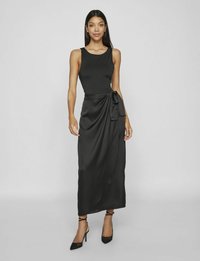 Abito maxi in satin nero con busto aderente, gonna avvolgente e dettaglio con fiocco laterale. Tessuto liscio e design senza maniche con scollatura rotonda.