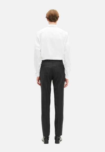 Camisa blanca de manga larga con corte recto, combinada con pantalones de cuadros gris oscuro. Incluye zapatos negros y textura suave.