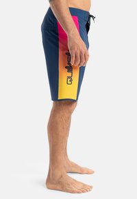 Męskie szorty kąpielowe w granatowym kolorze z gradientowym wzorem przechodzącym od różowego do żółtego. Regulowany pas, kieszeń boczna oraz detal z logo po bokach.