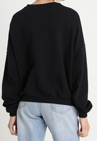 Black oversized sweatshirt with a round neck, dropped shoulder seams, and ribbed hem. Soft texture with minimal design details.