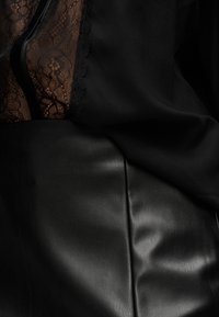 Μαύρη δερμάτινη φούστα συνδυασμένη με διάφανο ύφασμα με μαύρη δαντέλα και λείο μαύρο ύφασμα, αναδεικνύοντας αντιθέσεις υφής και λεπτομέρειες υφασμάτων.