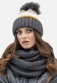 Knit gray beanie with a white and yellow band, topped with a faux fur pom-pom. Chunky gray knit scarf adds texture and warmth.
