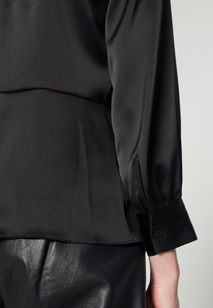 Black satin long sleeve top with buttoned cuff paired with black leather skirt, showing side and back detail on light background.