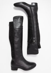 Botas negras hasta la rodilla que combinan cuero liso y ante. Detalle de cremallera en el lado interno y un tacón bajo.