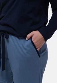 Marinblus med långa ärmar och rund halsringning, kombinerad med ljusblå byxor med sidfickor och dragsko i midjan. Strukturerad tyg.