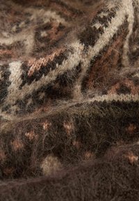 Stickad ulltyg i nyanser av brunt och kräm med en texturerad, mjuk yta och geometriska mönster genom hela tyget. Har ett varmt och mysigt utseende.
