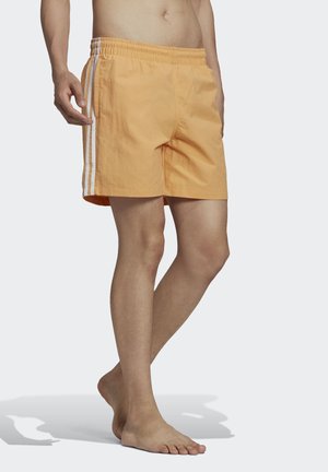 Pantaloni da bagno arancioni realizzati in materiale leggero con una vita elasticizzata, tasche laterali e strisce bianche lungo i lati.