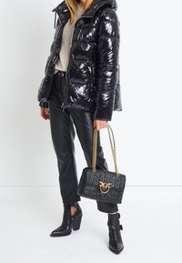 Černá, lesklá péřová bunda, šedý svetr, černé kožené kalhoty, boty na podpatku do kotníku. Černá kabelka s vyraženým vzorem a zlatou kovovou sponou.