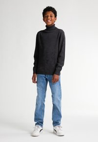 Schwarzer Rollkragenpullover mit strukturiertem Finish, kombiniert mit hellblauen Jeans und weißen Sneakers. Einfaches, klassisches Design.
