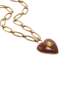 Serce w kształcie wisiorka wykonane z brązowej emalii z akcentem w postaci żółtego kamienia szlachetnego, zawieszone na łańcuszku w złotym odcieniu z wydłużonymi ogniwami.