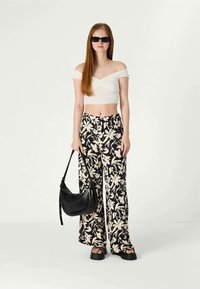 Black and white floral wide-leg pants, a white off-the-shoulder crop top, and a black shoulder bag. Features flat sandals and sunglasses.