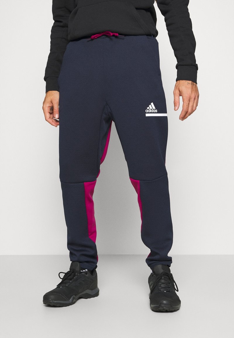 Marinblå joggerbyxor med rosa sidopaneler, elastisk midja med snörning och vit Adidas-logotyp på låret. Strukturerad tyg.