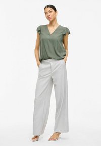 Blusa verde oliva de cuello en V con mangas acampanadas, combinada con pantalones de pierna ancha en gris claro y tacones blancos con tiras. Tejido suave y corte ajustado.