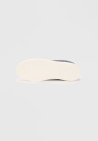 Semelle d'une sneaker, mettant en avant un fond en caoutchouc blanc texturé avec des rainures et une section supérieure grise pour la traction et le soutien.