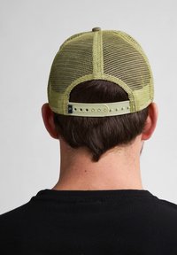 Gorra de malla verde con una correa ajustable de plástico en la parte posterior. Presenta una parte superior redondeada y una forma estructurada. El fondo es neutro.