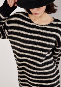 Sort og creme striped strikket sweater med en løs pasform, bred udskæring og ribbede manchetter. Stoffet har en fluffy tekstur og synlige sømme.