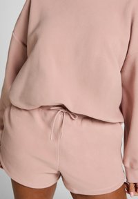 Lichtroze fleece loungewear set met een losse sweatshirt en shorts met trekkoord, zachte textuur en casual ontwerp.