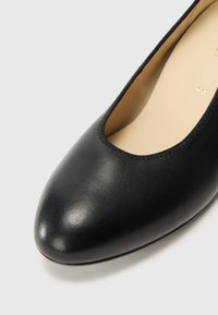 Sorte skinnballetsko med rund tå, lett glans og sydd detaljer rundt åpningen. Glatt innersåle.