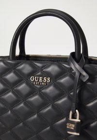 Borsa a tracolla nera trapuntata in pelle liscia, con logo dorato "GUESS", chiusura con zip e manici strutturati con una tracolla decorativa.