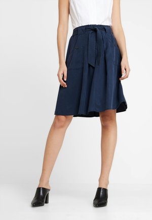 Laivaston sininen A-linjainen hame, jossa on solmittava vyö, taskut ja teksturoitu kangas. Ominaisuuksia ovat polven mittainen leikkaus ja sujuva laskostus.