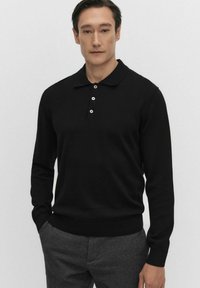 Czarna koszulka polo z długim rękawem, wykonana z dzianiny, z prążkowanymi mankietami i dolnym wykończeniem, zapinana na trzy guziki w białym kolorze, w połączeniu z szarymi spodniami.