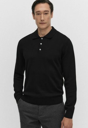 Svart långärmad polo, stickad material, ribbad manschetter och nederkant, tre-knapps knappslå med vita knappar, tillsammans med grå byxor.