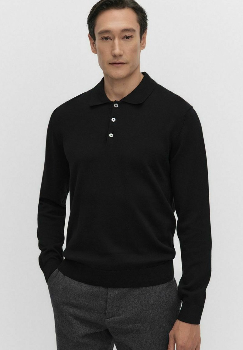 Czarna koszulka polo z długim rękawem, wykonana z dzianiny, z prążkowanymi mankietami i dolnym wykończeniem, zapinana na trzy guziki w białym kolorze, w połączeniu z szarymi spodniami.