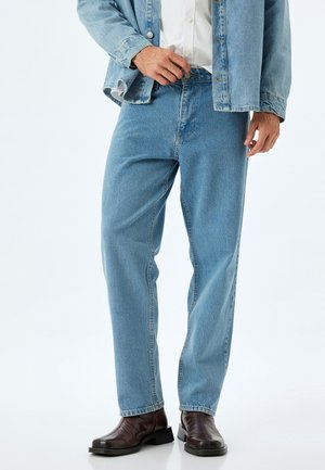 Slight blå denim jeans med lige ben, klassisk fem-lomme design og lynlås. Båret sammen med en lys blå denimjakke og brune støvler.