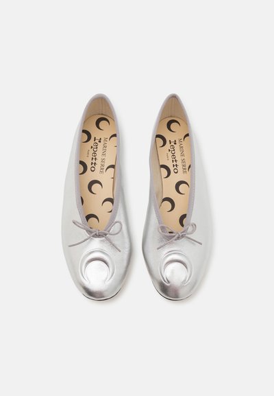 Silver leather ballet flats with small bows and crescent-shaped embellishments on the toes, paired side by side on a white background.
