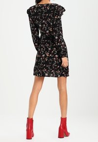 Robe noire à fleurs avec des épaules froncées et des manches longues, ornée de fleurs multicolores. Portée avec des bottines à talons carrés rouges.