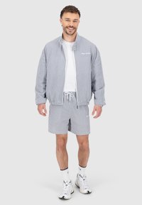 Veste rayée et short en bleu et blanc, en tissu léger ; dispose d'une fermeture éclair, d'une taille à cordon de serrage et d'un logo brodé.