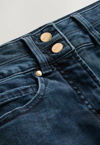 Mörkblå denimjeans med en klassisk femficksdesign, dubbla metallknappar och synliga sömdekorationer.