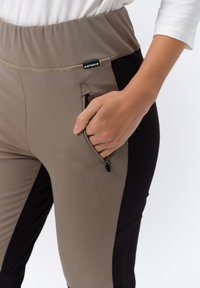 Brown and black athletic pants with a wide waistband. Features a zippered pocket on the right side and smooth fabric texture.