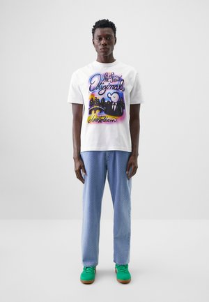 White cotton t-shirt with colorful "Amsterdam" graphic, paired with light blue patterned pants and green sneakers with brown soles.