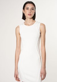 Robe blanche sans manches avec une texture côtelée et des accents en dentelle sur les côtés, présentant une silhouette ajustée et un col rond.