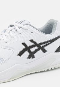 Weißer Sportschuh mit strukturierter Oberseite, schwarzen Logofarben und grauem Besatz. Verfügt über eine traditionelle Schnürung und eine gepolsterte Sohle.