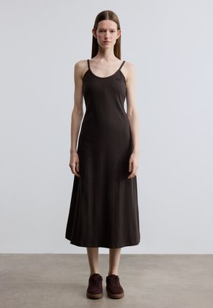 Zwarte geribbelde midi-jurk met dunne bandjes en een ronde hals, met een gestroomlijnde silhouet. Gecombineerd met donker bordeauxrode sneakers.