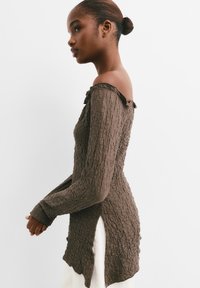 Top lungo a maniche con texture marrone e design off-the-shoulder; presenta un collo arricciato e una silhouette aderente con spacchi laterali.