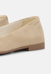 Bailarinas de ante beige con un bajo tacón marrón, que presentan un diseño simple y un upper texturizado. El interior tiene un forro de tela a rayas.