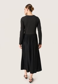 Black dress features a fitted long-sleeve top and a pleated skirt. Fabric appears smooth on top, with textured pleats below.
