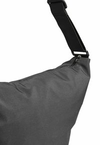 Zwarte stoffen crossbody tas met ritssluiting en verstelbare riem op een witte achtergrond.