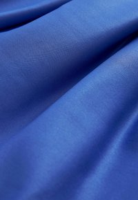 Satiinikangas syvän sinisessä värissä, jolla on sileä ja kiiltävä pinta, laskostettuna näyttämään taitoksia ja pintakiiltoa.