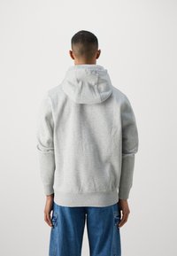 Sudadera gris hecha de una tela suave, con capucha ajustable, puños acanalados y dobladillo. La vista posterior muestra un diseño liso sin gráficos.