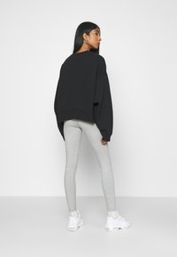 Felpa nera oversize con maniche lunghe, abbinata a leggings grigi chiari e sneakers bianche. Design semplice con una vestibilità rilassata.