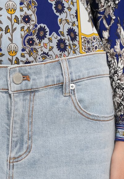 Blugi din denim de culoare bleu deschis, cu talie medie, având cusături din cupru și un nasture argintiu, asortați cu un top dintr-o țesătură cu model.