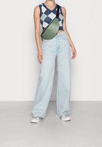 Vihreä tekonahkainen olkalaukku vetoketjulla, säädettävä musta hihna, käytetty sinivalkoisen argyle-kuvioisen crop topin ja korkeavyötäröisten vaaleiden farkkujen kanssa.